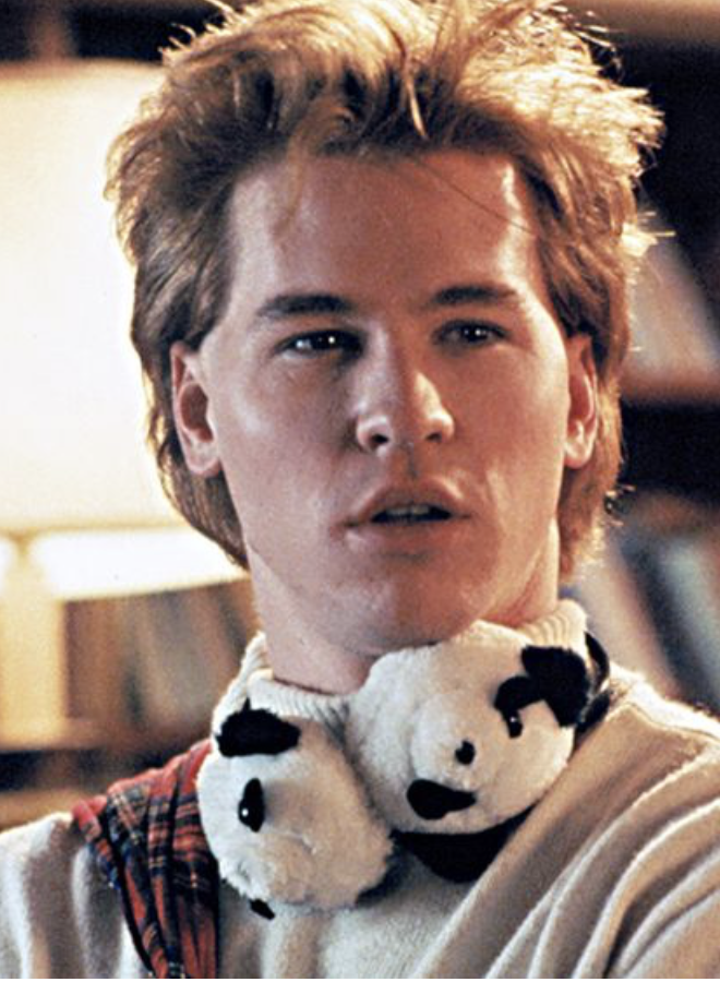 Val Kilmer from Real Genius with panda ear muffs around his neck looking confused.
